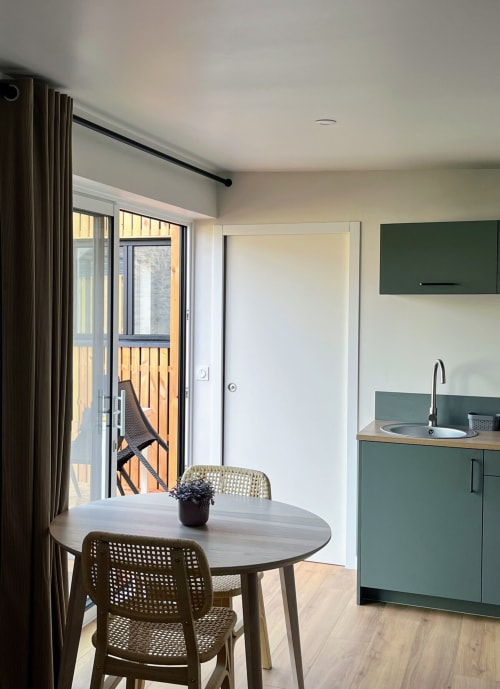 Appartement studio moderne aux Logis du canal avec table ronde, kitchenette, mobilier vert et accès balcon