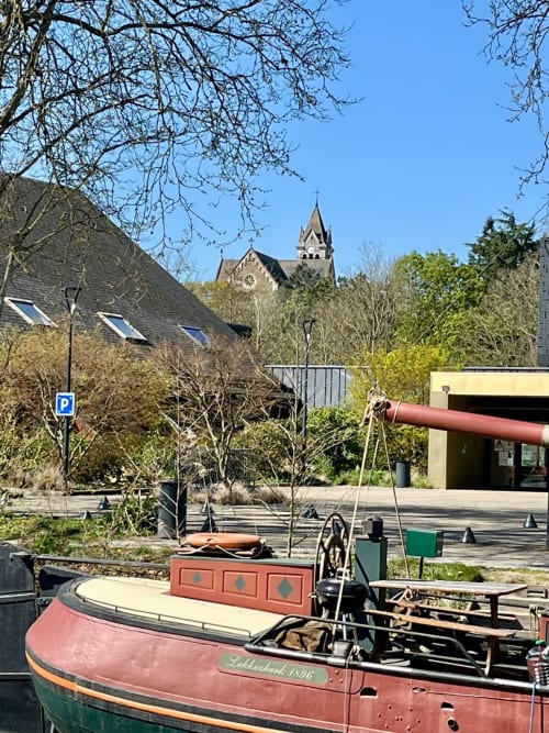 Bateau vintage amarré aux Logis du canal à Betton, France, avec le clocher et les bâtiments en arrière-plan