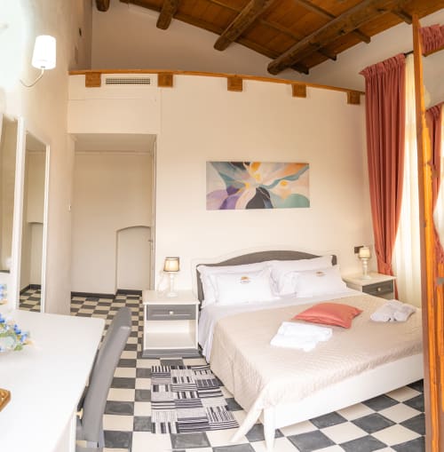Camera matrimoniale moderna all'Albergo Al Cinghiale di Guspini con letto queen, pavimento in piastrelle a quadri, travi in legno a vista e