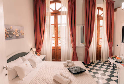 Camera doppia deluxe dell'Albergo Al Cinghiale con eleganti tende rosse, porte in legno, pavimento a scacchiera e biancheria bianca