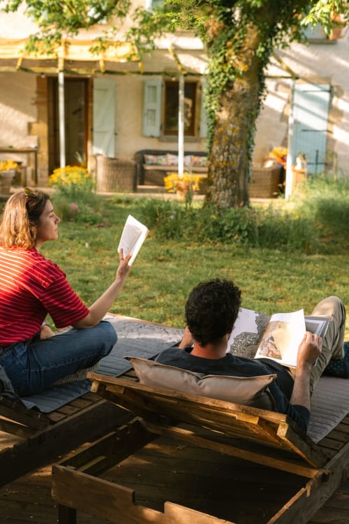 Couple se relaxant dans des chaises longues lisant à la chaumière Domaine Langelet à Saint-Gauzens, entouré de lierre et terrasse