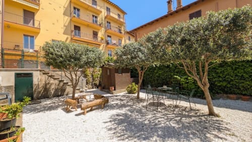 Soleggiato cortile con ulivi, sedute e edifici gialli italiani - appartamento Villa Italia Management