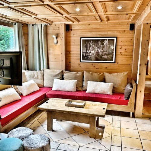 Cozy wooden chalet living room with red cushioned seating, fireplace, TV, and garden view at Chez Francine