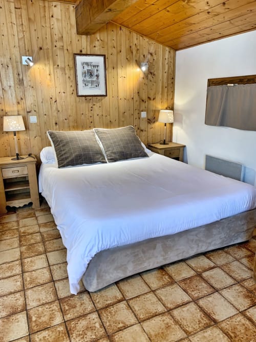 Cozy wood-paneled studio bedroom at Chez Francine with queen bed, white linens, checkered pillows, and terra cotta tile