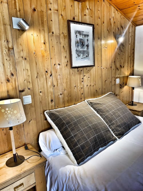 Cozy wood-paneled studio bedroom at Chez Francine with dark plaid pillows, lamp, and framed artwork on walls.