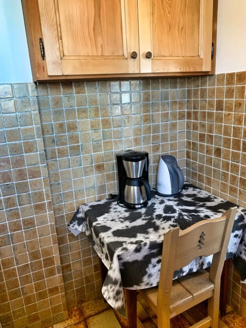Kitchen corner with coffee maker and kettle on cow-print cloth, wooden cabinets, tiled backsplash at Chez Francine apartment