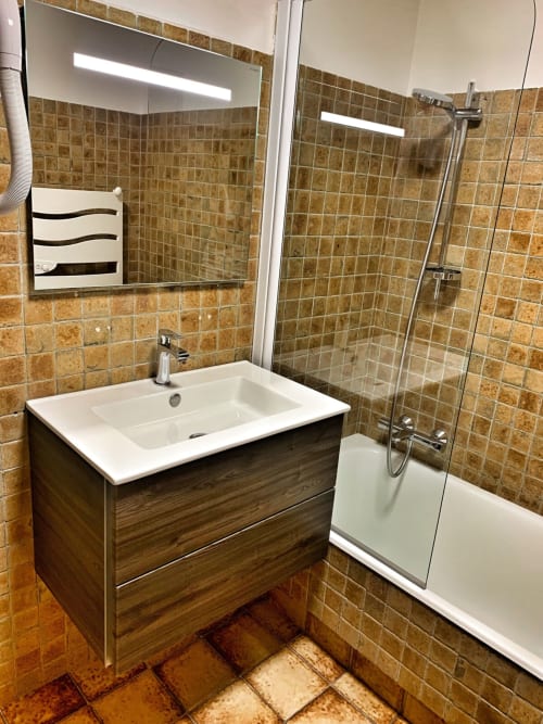 Modern bathroom in Chez Francine apartment with wooden vanity, white sink, mirror, and walk-in shower with terracotta tiles
