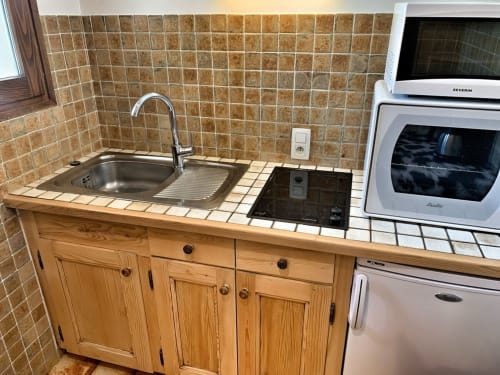 Studio kitchen with wooden cabinets, tiled backsplash, sink, cooktop, microwave, and oven at Chez Francine apartment