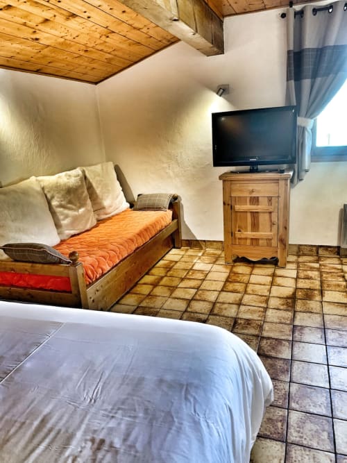 Studio Reguet bedroom at Chez Francine with wooden bed, TV, terracotta tile floor, and exposed beam ceiling in Notre Dame de