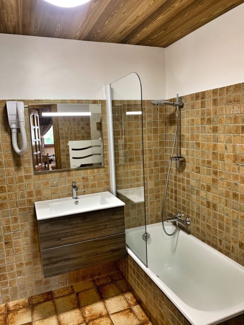 Modern bathroom with brown tile walls, white sink vanity, bathtub with glass shower enclosure at Studio Reguet, Chez Francine