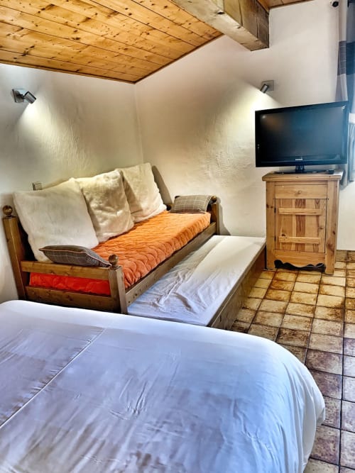 Studio bedroom at Chez Francine with wooden ceiling, TV, twin beds with orange and white bedding, and wooden furniture in