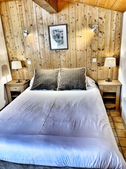 Cozy wood-paneled bedroom at Chez Francine with white bedding, plaid pillows, and wooden nightstands with lamps.