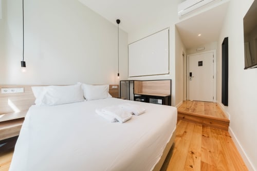 Modern Premium Suite bedroom at GS Chiado Boutique Studios in Lisbon with white bed, wooden floors, and city view window