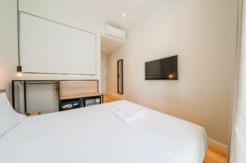 Modern premium suite bedroom at GS Chiado Boutique Studios in Lisbon with white bed, flat-screen TV, and minimalist decor