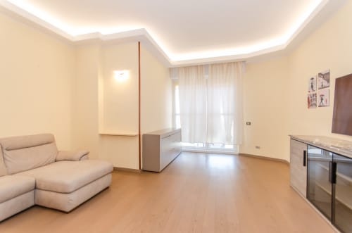Soggiorno moderno a Milano con divano beige, pavimento in legno, angolo cottura e illuminazione ambientale