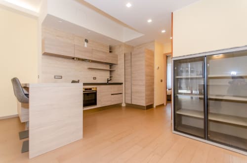 Cucina di moderno appartamento milanese con mobili in legno chiaro, isola centrale e frigorifero con vetrina espositiva