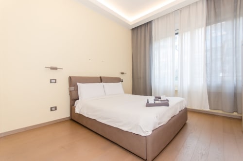 Camera moderna presso Milano Hospitality Porta Nuova Home con letto matrimoniale, biancheria bianca, pareti beige, pavimento in legno e ampia finestra