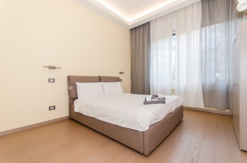 Camera moderna presso Milano Hospitality's Porta Nuova Home con letto marrone, biancheria bianca, pareti color crema e luce naturale