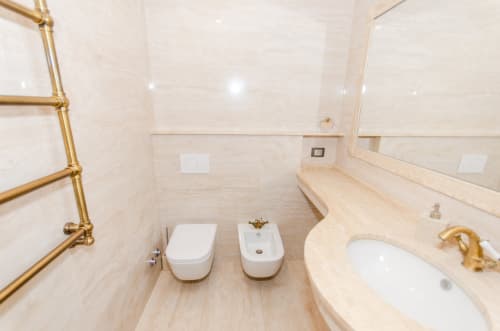 Bagno moderno in appartamento milanese con piastrelle di marmo, wc, bidet, lavabo curvo e rubinetteria dorata