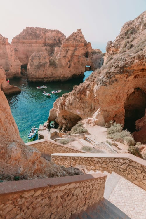Enseada dramática com falésias vermelhas, águas turquesas e barcos de pesca no Algarve português