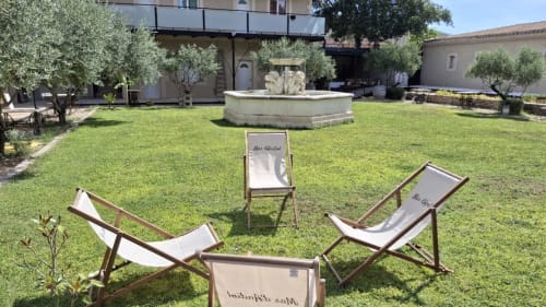 Jardin ensoleillé de Le Mas d'Andiol avec chaises longues, fontaine centrale et bâtiments en pierre à Plan d'Orgon