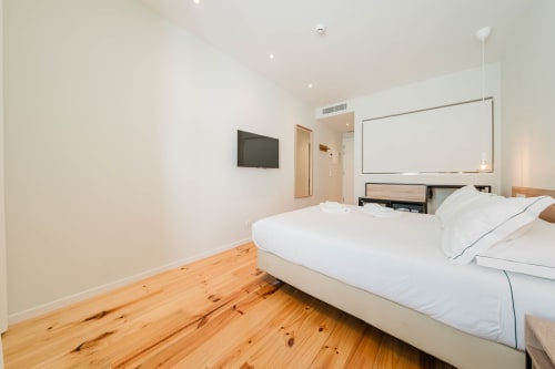 Quarto duplo moderno no Hotel Liberator Rossio com piso de madeira, roupa de cama branca, TV e mobiliário contemporâneo