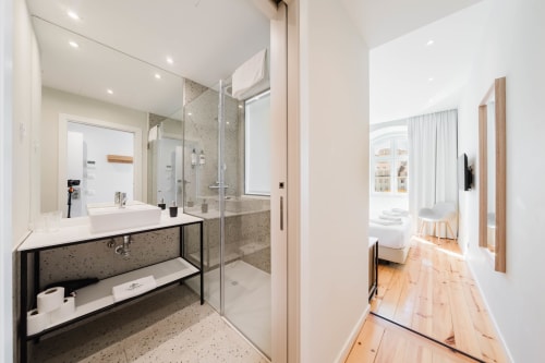 Banheiro moderno no Hotel Liberator Rossio Lisboa com chuveiro tipo chuva, lavatório em mármore e piso em madeira conectando ao quarto.