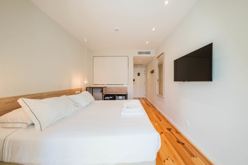 Quarto moderno do Hotel Liberator Rossio Lisboa com cama de madeira, roupa branca, TV de tela plana e decoração minimalista