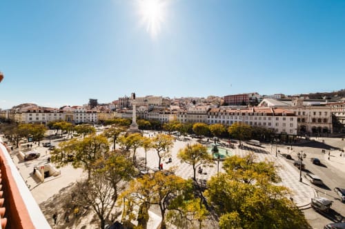 Dia ensolarado em Lisboa com vista para a Praça do Rossio desde o Hotel Liberator Rossio, com arquitetura histórica e árvores visíveis