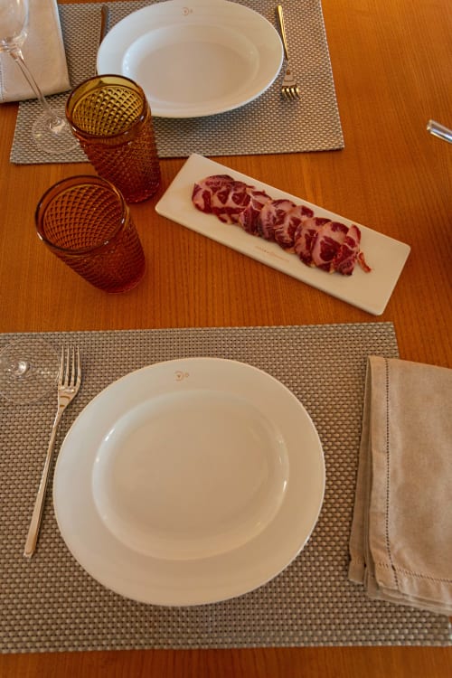Mesa elegante em Cerro da Campaniça com pratos brancos, talheres dourados, copos âmbar e carne curada fatiada em madeira