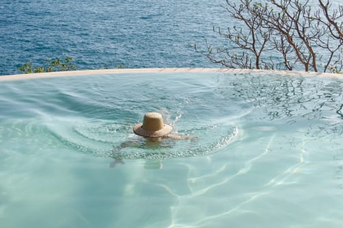 Persona nadando en el mar turquesa de Casa Baori, Puerto Ángel, con sombrero de paja y mangles y playa visibles.