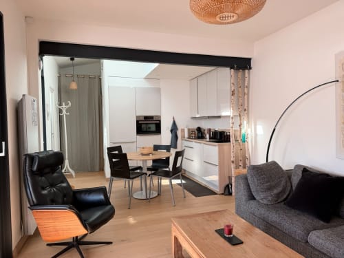 ARLOÉ La Rochelle : Studio moderne décloisonné avec fauteuil cuir noir, canapé gris, table à manger, kitchenette et bois
