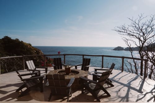 Terraza frente al océano en Casa Baori, Puerto Ángel, con sillas Adirondack negras, fogata y vistas al mar turquesa