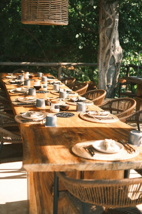 Mesa de comedor de madera con sillas tejidas lista para la comida en Casa Baori, Puerto Ángel, rodeada de exuberante vegetación