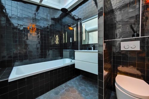 Salle de bain moderne aux carreaux noirs de l'appartement O LIT avec baignoire, douche, lavabo, toilettes et chauffage au sol