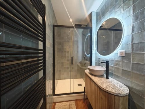 Salle de bains moderne de l'appartement O LIT avec sèche-serviettes chauffant, miroir lumineux, vasque blanche et douche vitrée