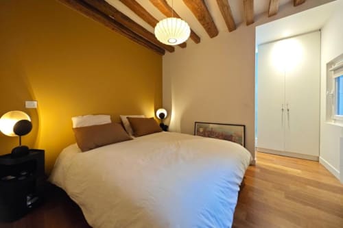 Chambre moderne de l'appartement O LIT avec poutres en bois apparent, literie blanche, mur d'accent jaune et parquet en France