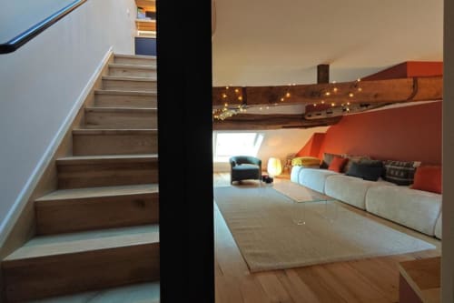 Loft moderne à O LIT avec escalier en bois, canapé crème, mur d'accent orange, poutres apparentes et guirlandes lumineuses