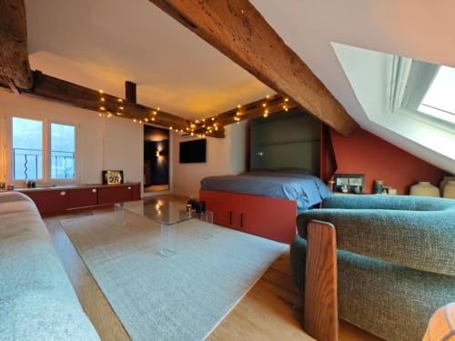 Chambre loft moderne à l'hôtel O LIT avec poutres apparentes, lit rouge, canapé gris, guirlandes lumineuses et vue sur la ville