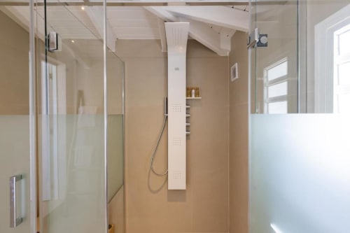 Salle de bain moderne avec douchette à effet pluie, étagères colonnaires blanches et murs carrelés beige à la villa O LIT