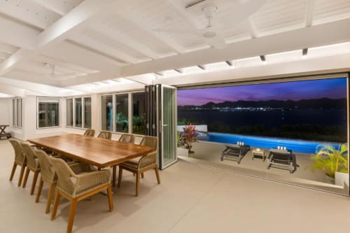 Villa contemporaine avec vue océan au crépuscule, table en bois, chaises tissées et piscine privée illuminée