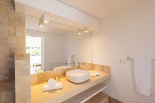 Salle de bain moderne de la villa O LIT avec vasque, grand miroir, plan de travail en marbre jaune et douche carrelée avec fenêtre