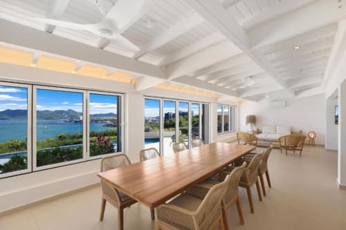 Salle à manger de villa de luxe avec table en bois, vue sur la baie, plafond à caissons blanc et mobilier côtier à O LIT