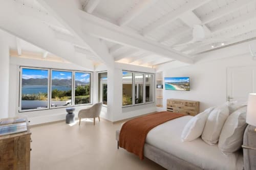 Chambre lumineuse avec vue sur mer, plafond à poutres blanches, lit king-size, commode en bois et baies panoramiques surplombant la Méditerranée