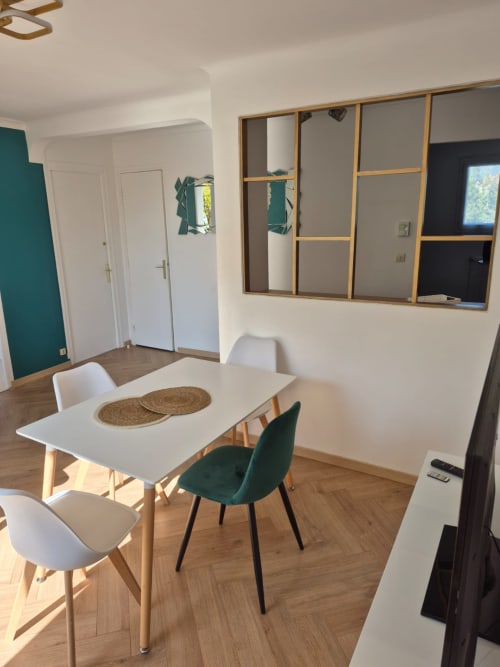 Salle à manger contemporaine de l'appartement La Parenthèse à Accolade Châteaudun avec table blanche, chaises en bois et mur à miroir