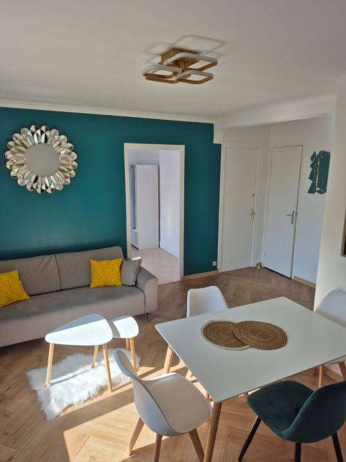 Séjour moderne avec mur d'accent bleu-vert, canapé gris, table à manger et parquet chez Accolade Châteaudun