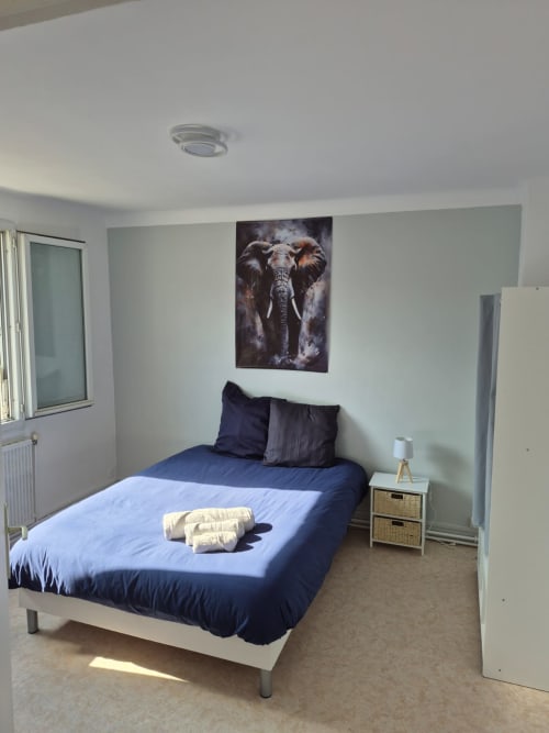 Chambre moderne de l'appartement La Parenthèse à l'hôtel Accolade, Châteaudun avec literie bleue et œuvre d'art éléphant