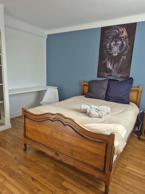 Lit en bois aux oreillers noirs dans l'appartement La Parenthèse de l'hôtel Accolade à Châteaudun, mur d'accent bleu et œuvre de lion
