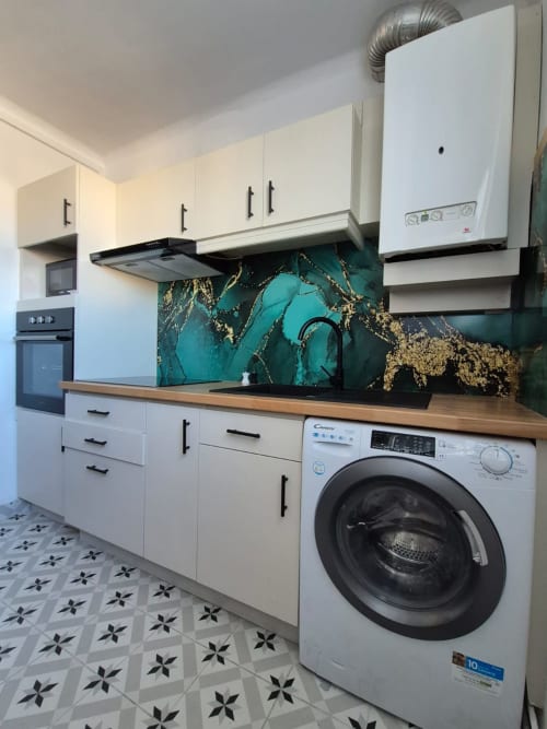 Cuisine moderne avec dosseret en marbre turquoise, armoires blanches, comptoir en bois, lave-linge et sol à motifs