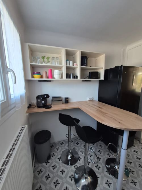 Kitchenette moderne de l'appartement La Parenthèse à l'hôtel Accolade, Châteaudun, avec comptoir en bois et tabourets de bar noirs